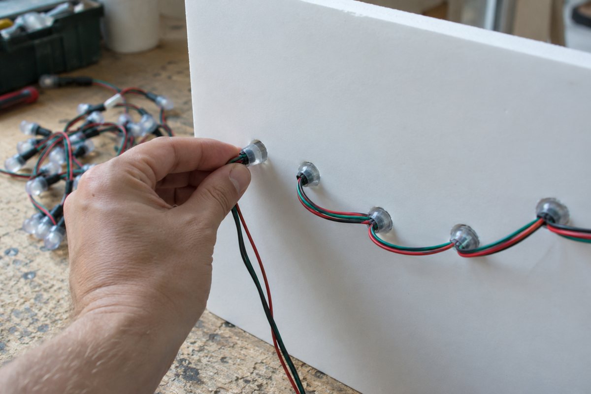 Illustration of the planned build: A hand pushing a pixel bulb into a hole from the back of the board.